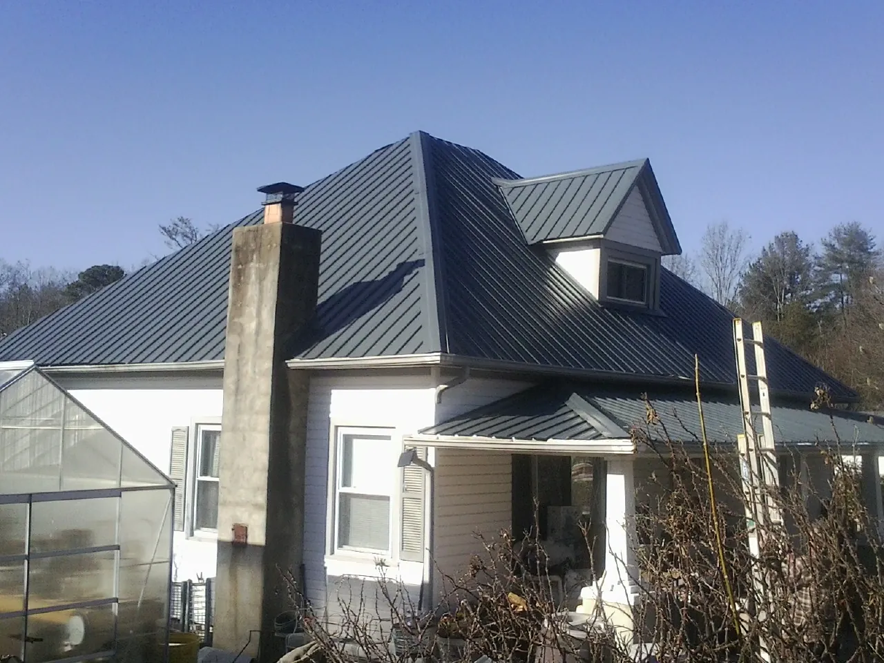 Dark blue standing seam metal roof on a white farmhouse with dormer — Slate & Tile Roof Repair by Roofing Brothers in Wampsville