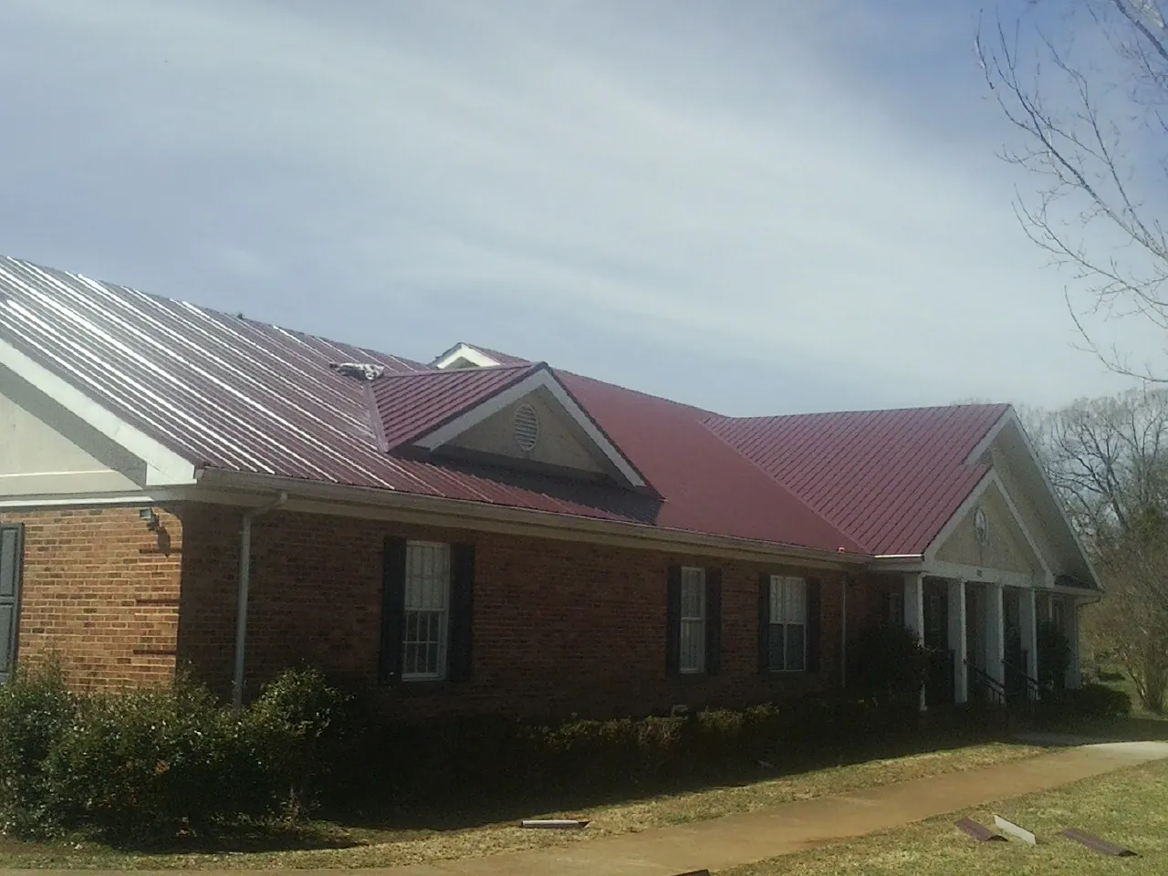 Red metal roof with gabled entries on a long brick building, from a Hail Damage Roof Repair job in Wampsville