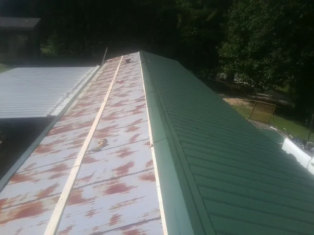 Old rusted panels beside newly installed green metal roofing — Wind Damage Roof Repair by Roofing Brothers in Wampsville
