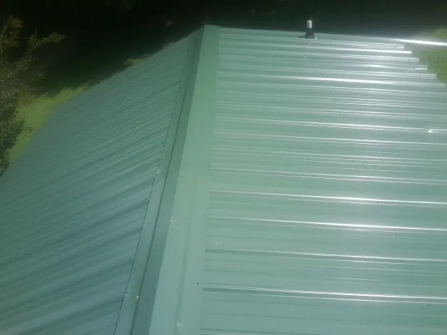 New green metal panels meeting at the ridge of a roof — Flat Roof Repair work by our crew in Wampsville