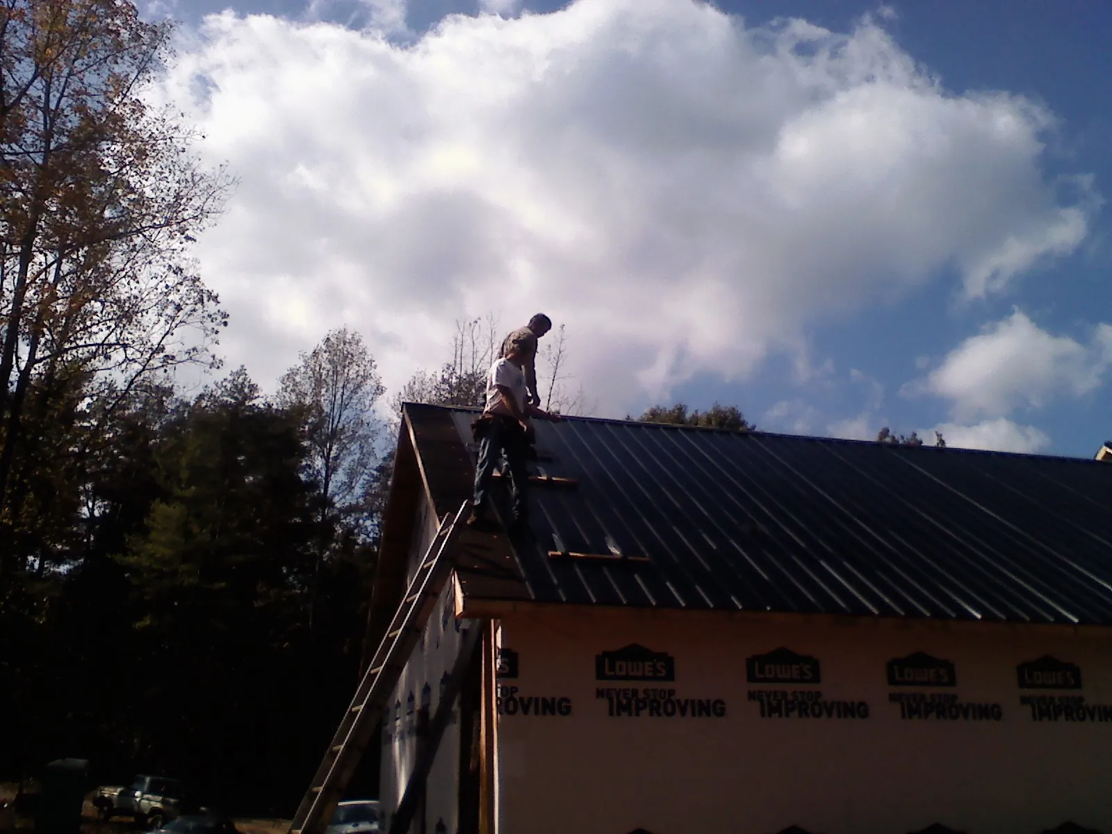 Roofer fastening dark metal panels high against a cloudy sky, from a Roof Inspection job in Wampsville