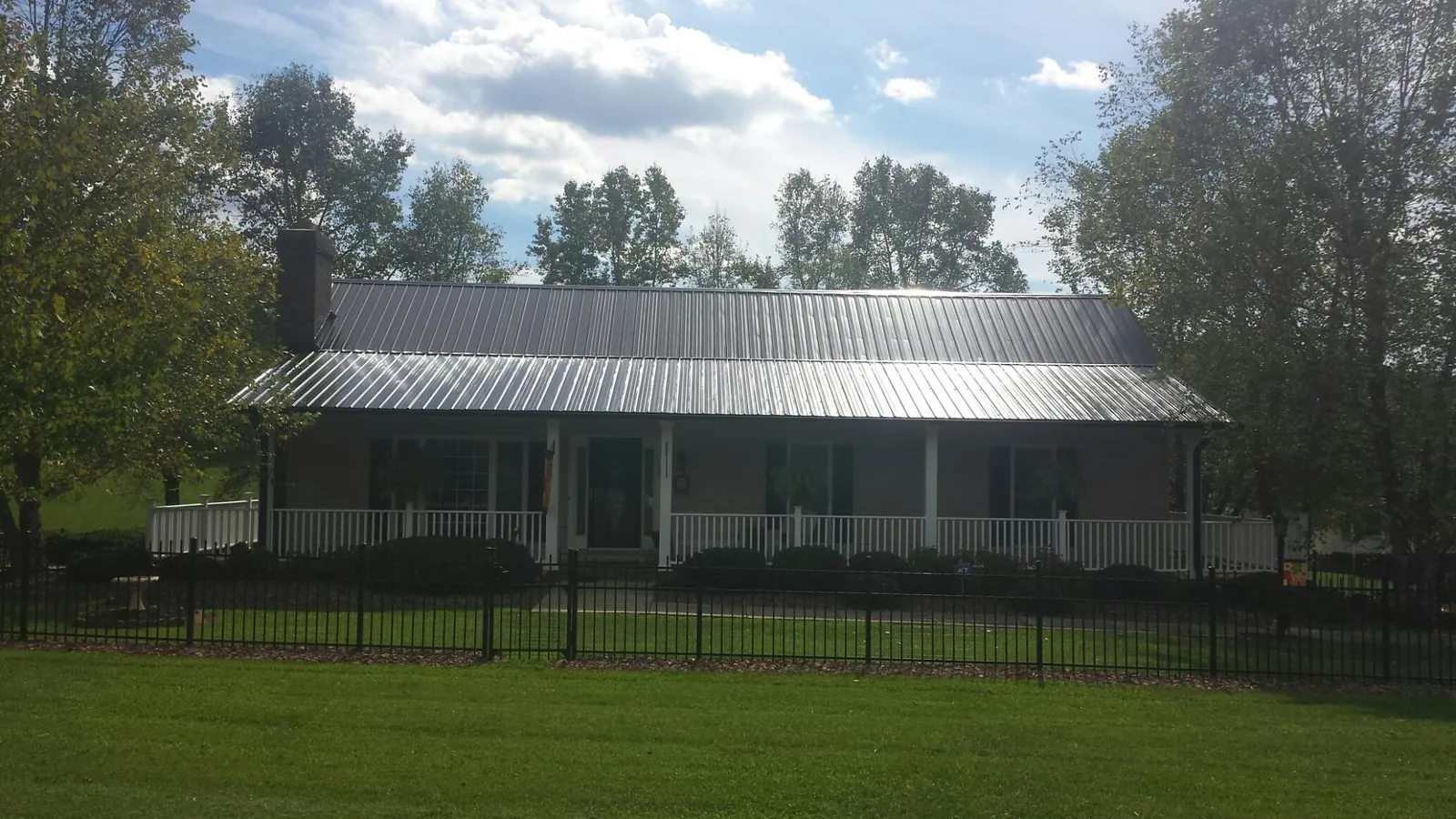 Gray metal roof on a brick ranch with a full width front porch — Gutter Guard Installation work by our crew in Wampsville