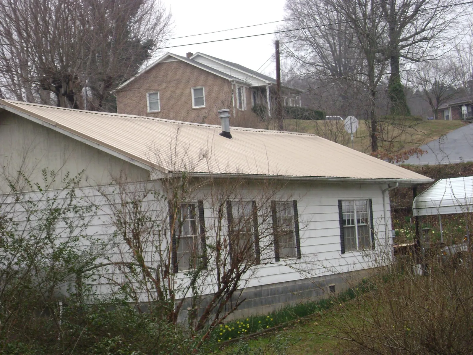 Tan metal roof on a white sided house set into a hillside — Commercial Roofing by Roofing Brothers in Wampsville