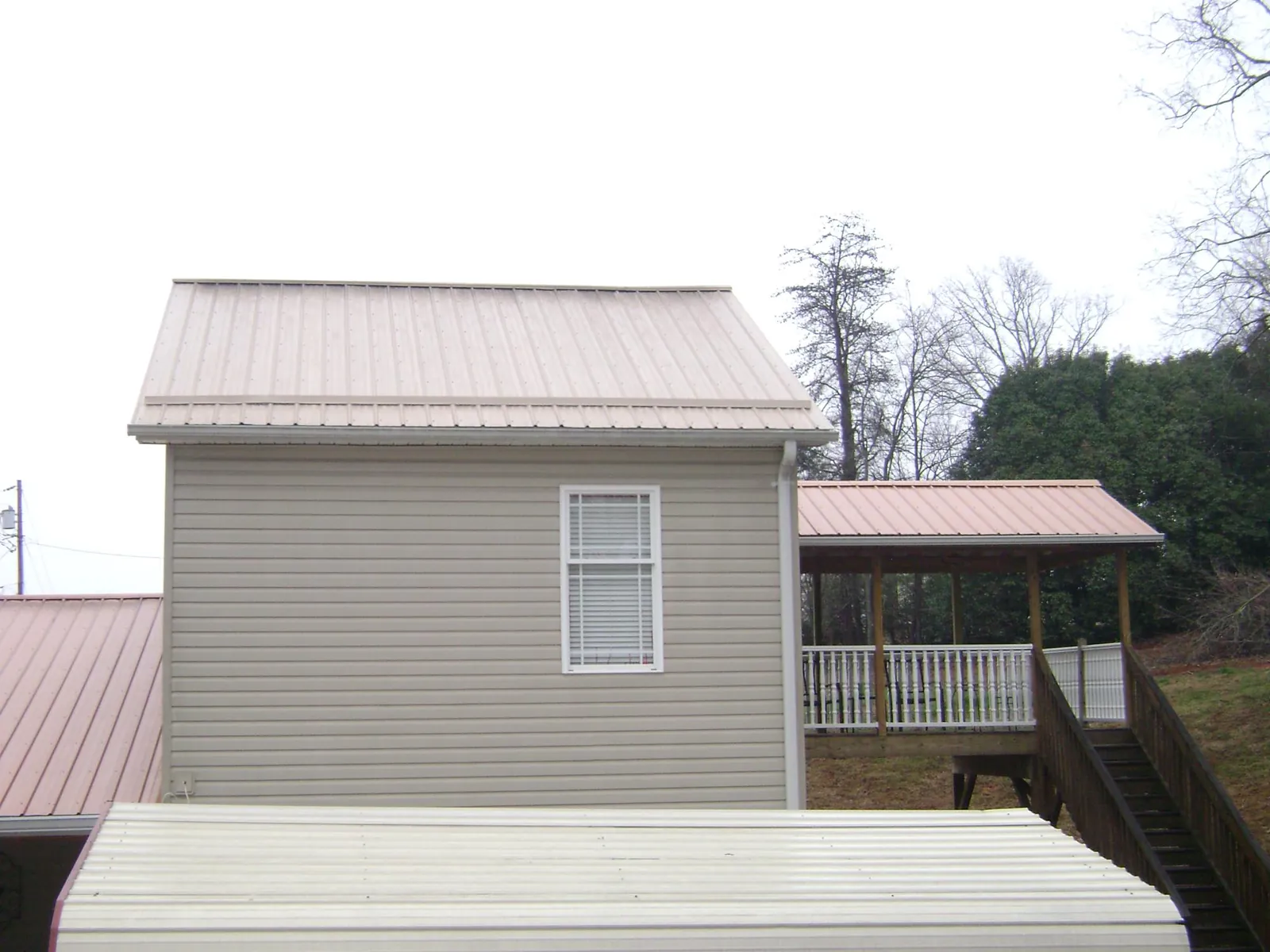 Tan metal roofs on a two story addition and attached porch, from a Roof Replacement job in Wampsville